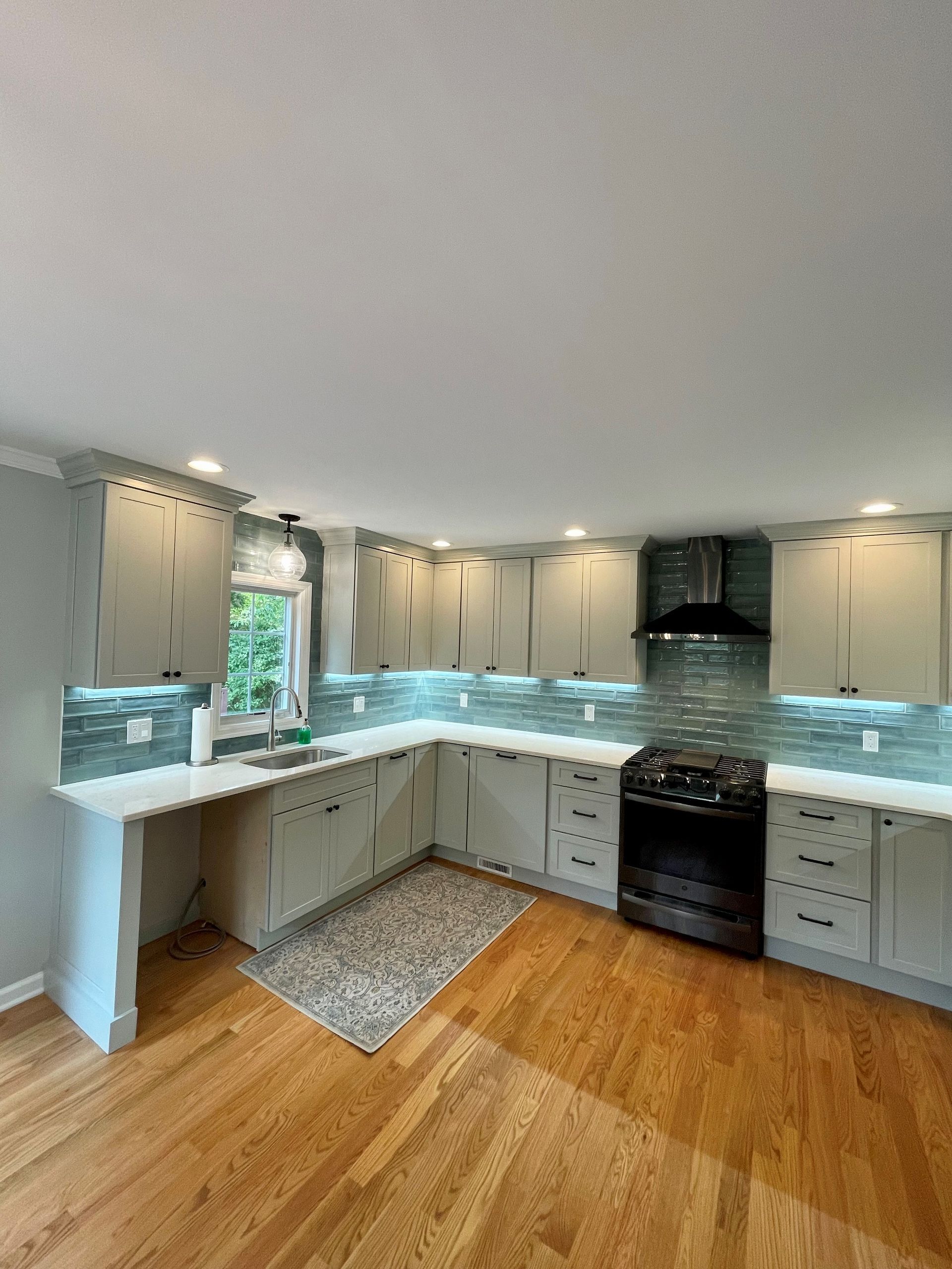 A kitchen with white cabinets, hardwood floors, a stove, and a sink.