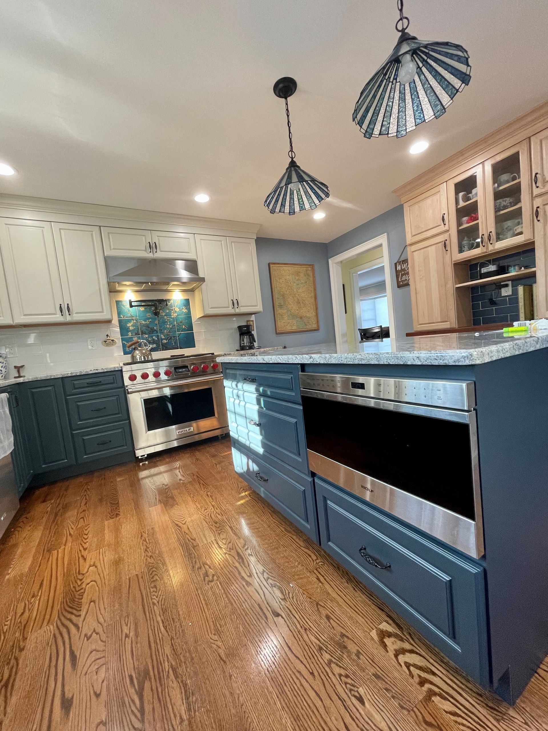A kitchen with blue cabinets, stainless steel appliances, and hardwood floors.