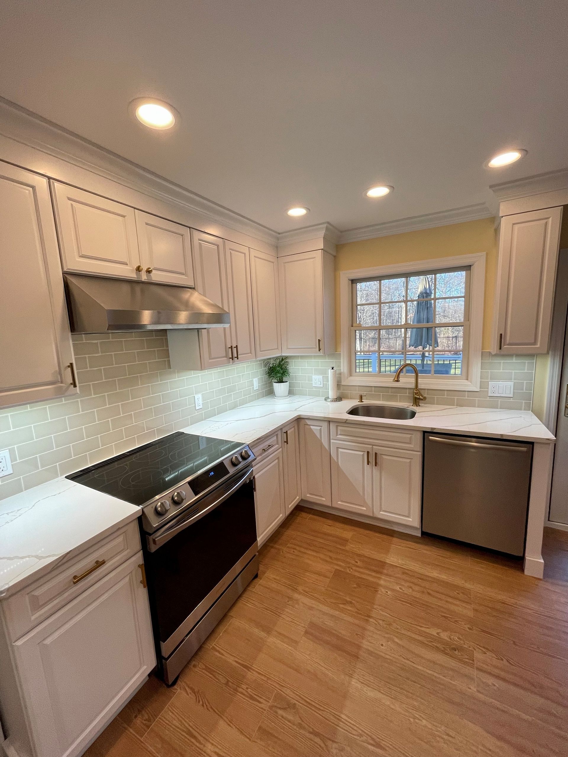A kitchen with white cabinets, a stove, a sink, and a window.