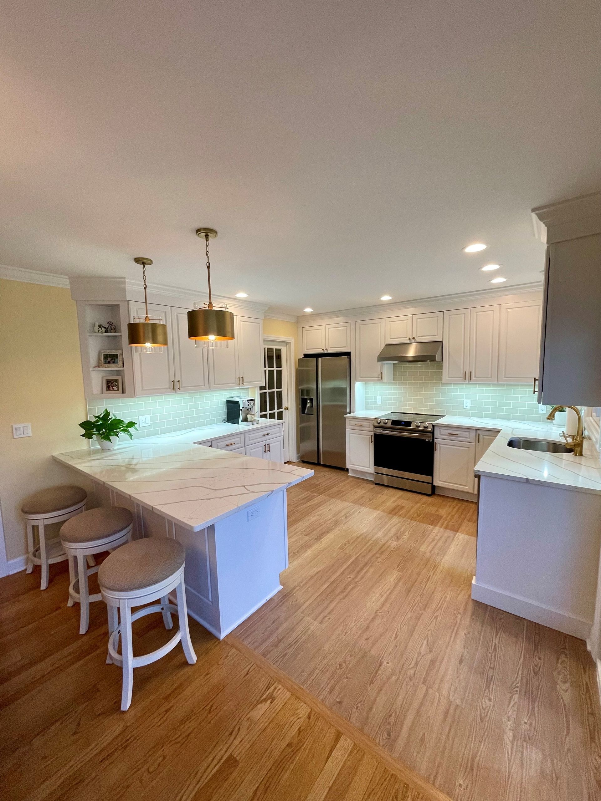 A kitchen with white cabinets, stainless steel appliances, hardwood floors, and a large island.
