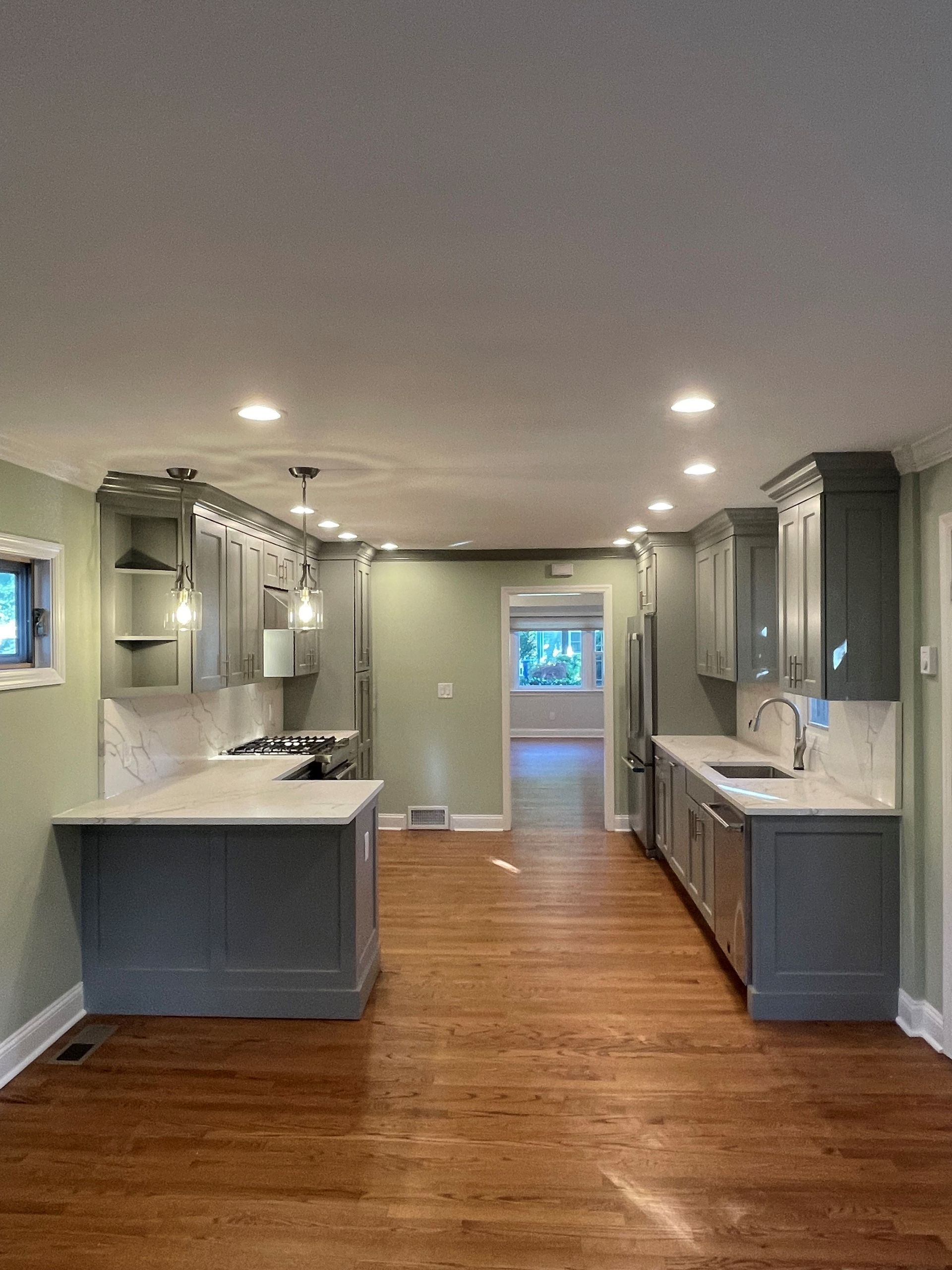An empty kitchen with hardwood floors and gray cabinets.