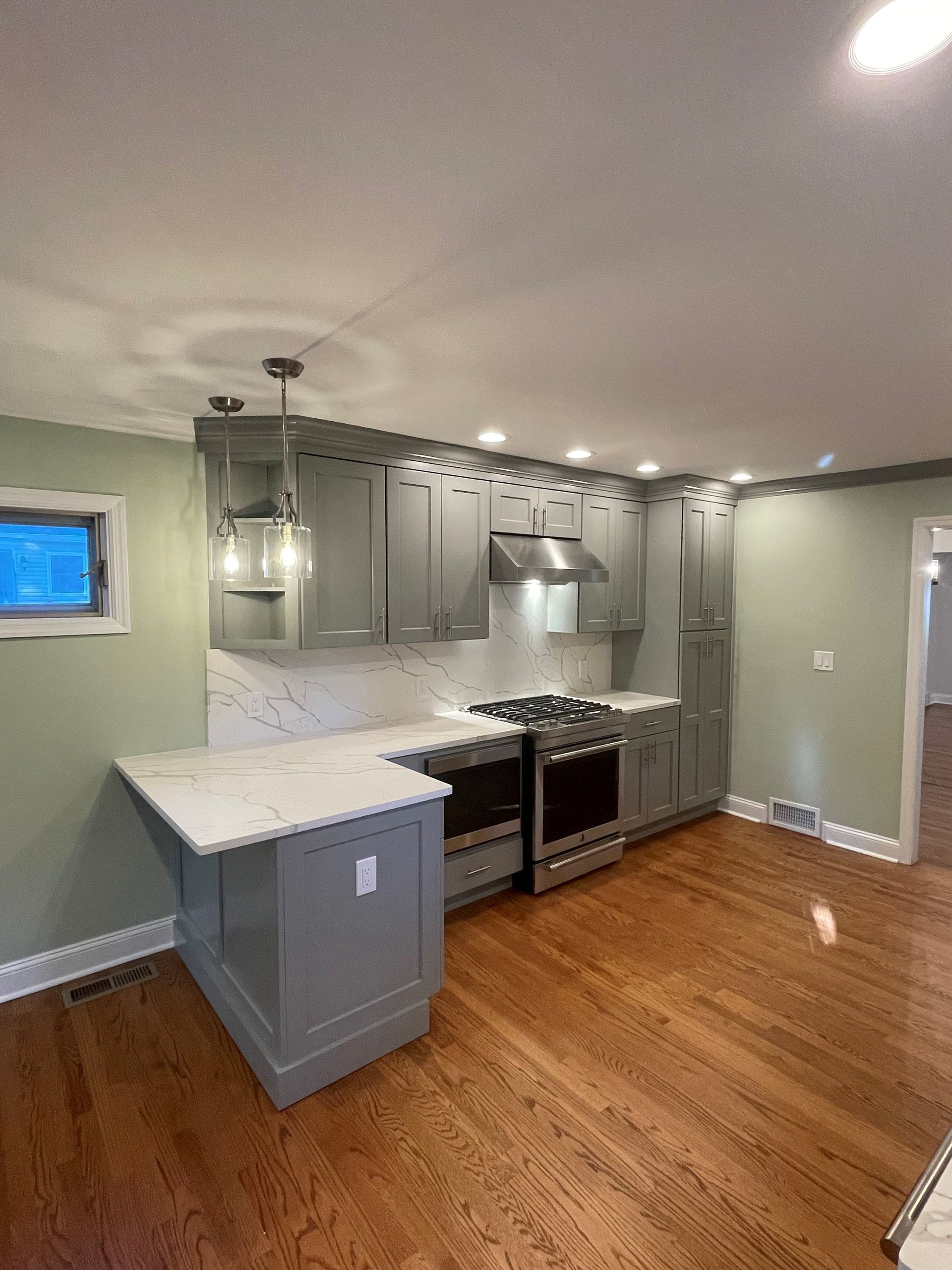 A kitchen with wooden floors, gray cabinets, a stove, and a window.