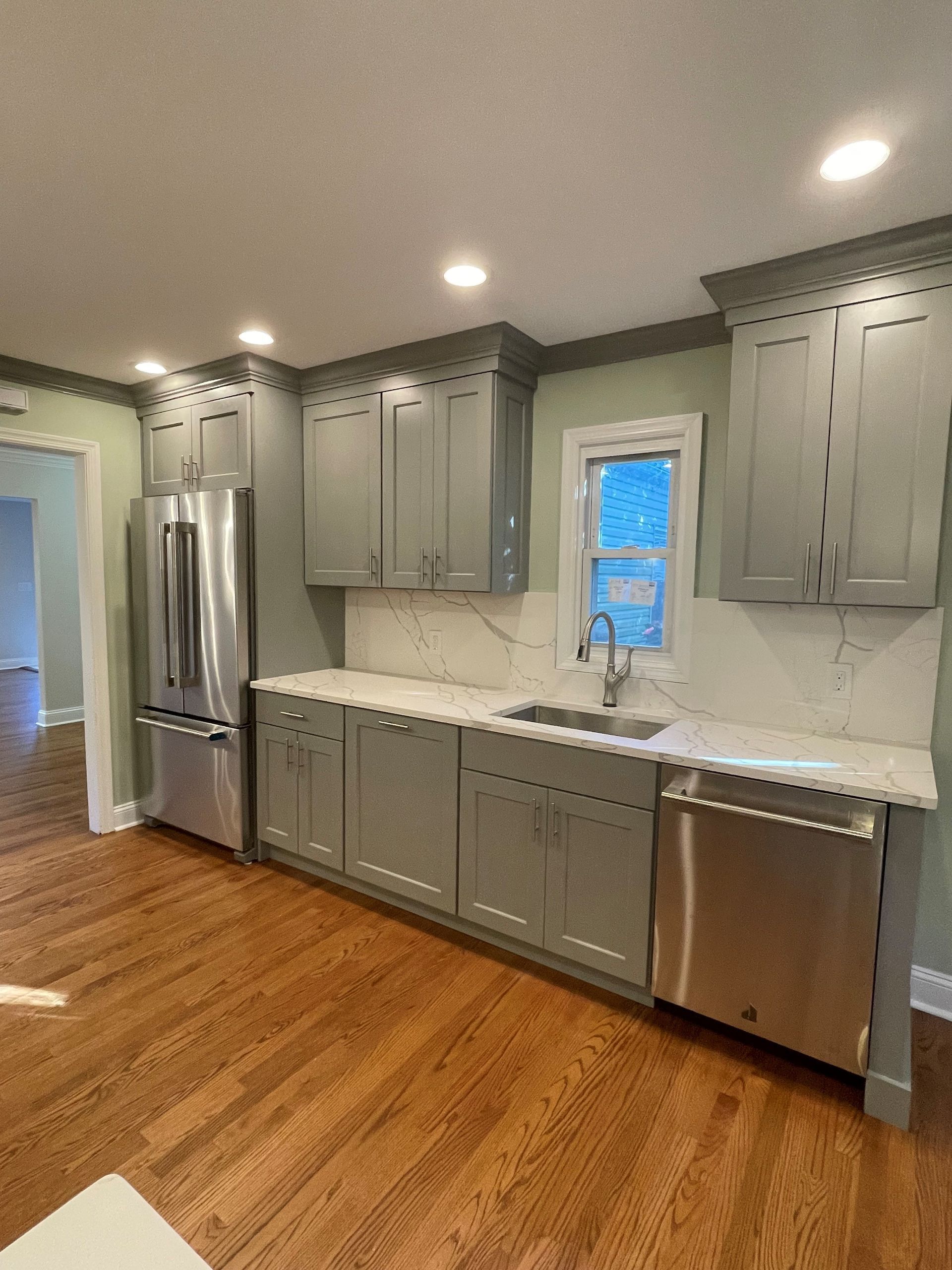 A kitchen with gray cabinets, stainless steel appliances, a sink, and a refrigerator.