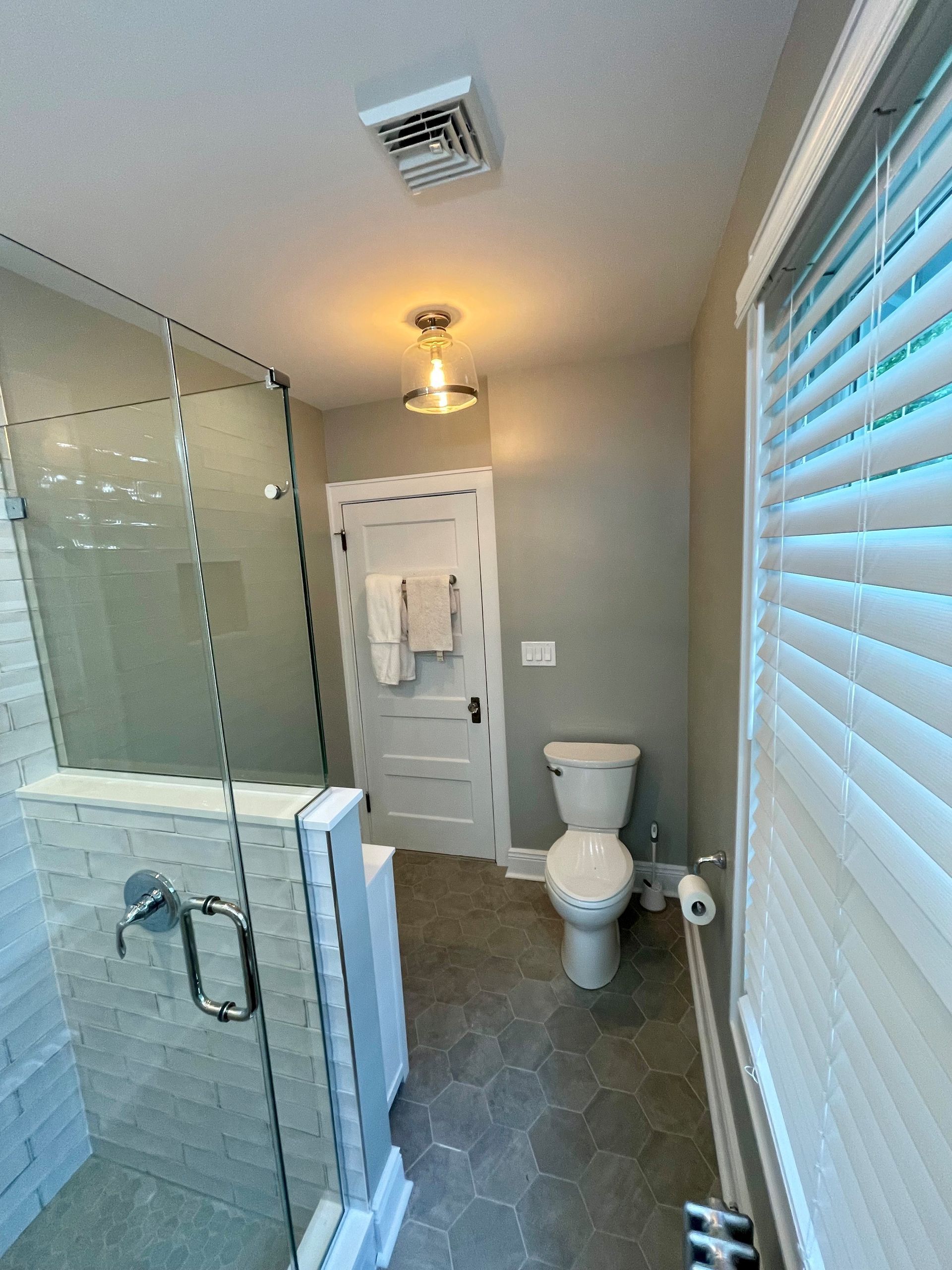 A bathroom with a toilet, shower, and window.