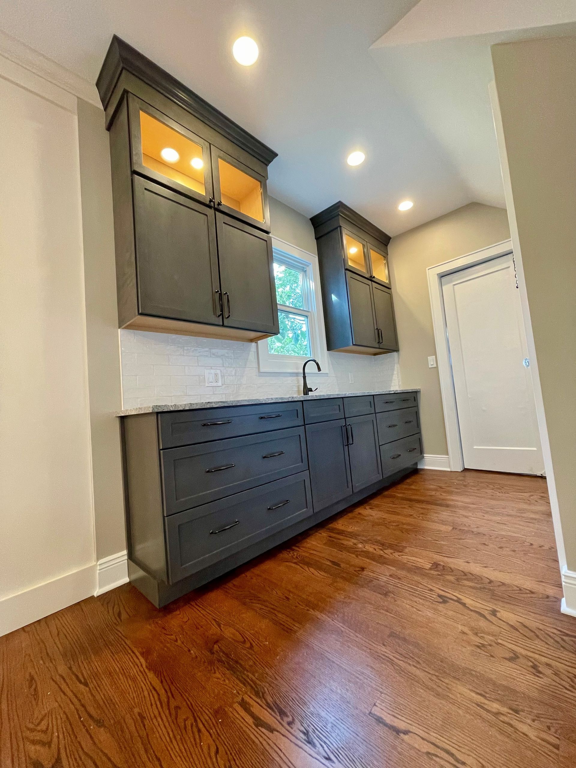 A kitchen with a sink, cabinets, and hardwood floors.