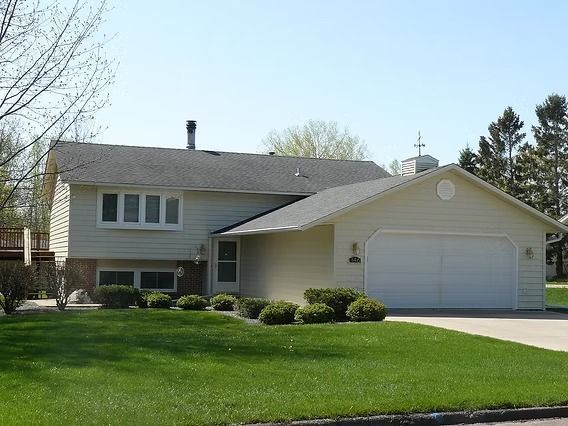 Beige split-level house with attached garage, green lawn, and blue sky.