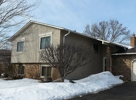 Two-story house with beige siding, brick base, and a snow-covered yard.