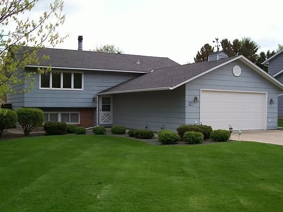 Blue house with a two-car garage, front lawn, and neatly trimmed bushes.