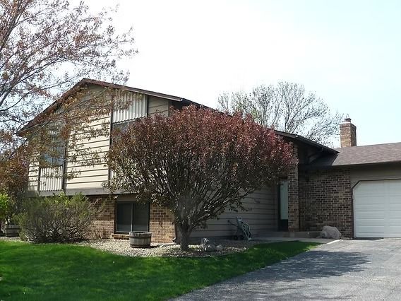 Two-story house with tan siding, a red-leafed tree in front, and a brick chimney and garage.