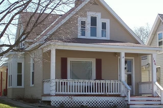 Beige two-story house with porch and red shutters.