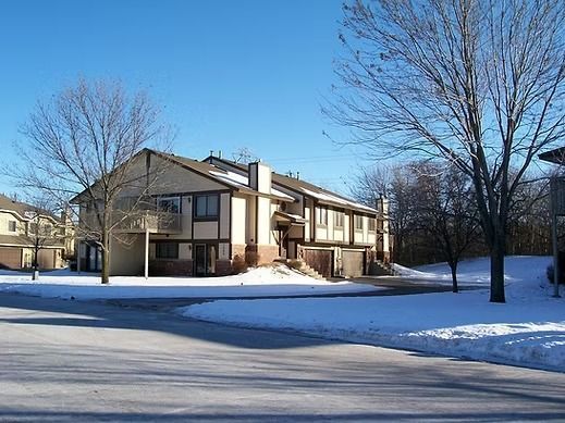 two-story tan and brown building with snow-covered ground and bare trees under a blue sky