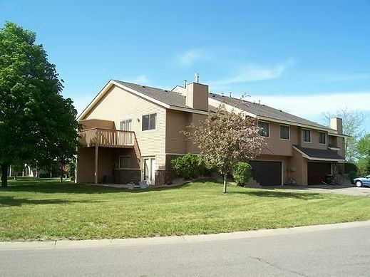 tan multi-unit building with brown roof, green lawn, and blue sky
