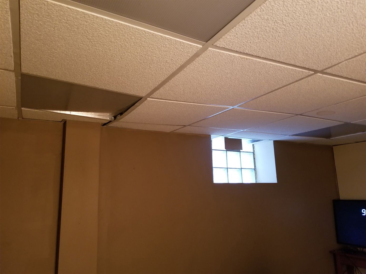 Basement ceiling with dropped tiles, tan walls, and a small glass block window.