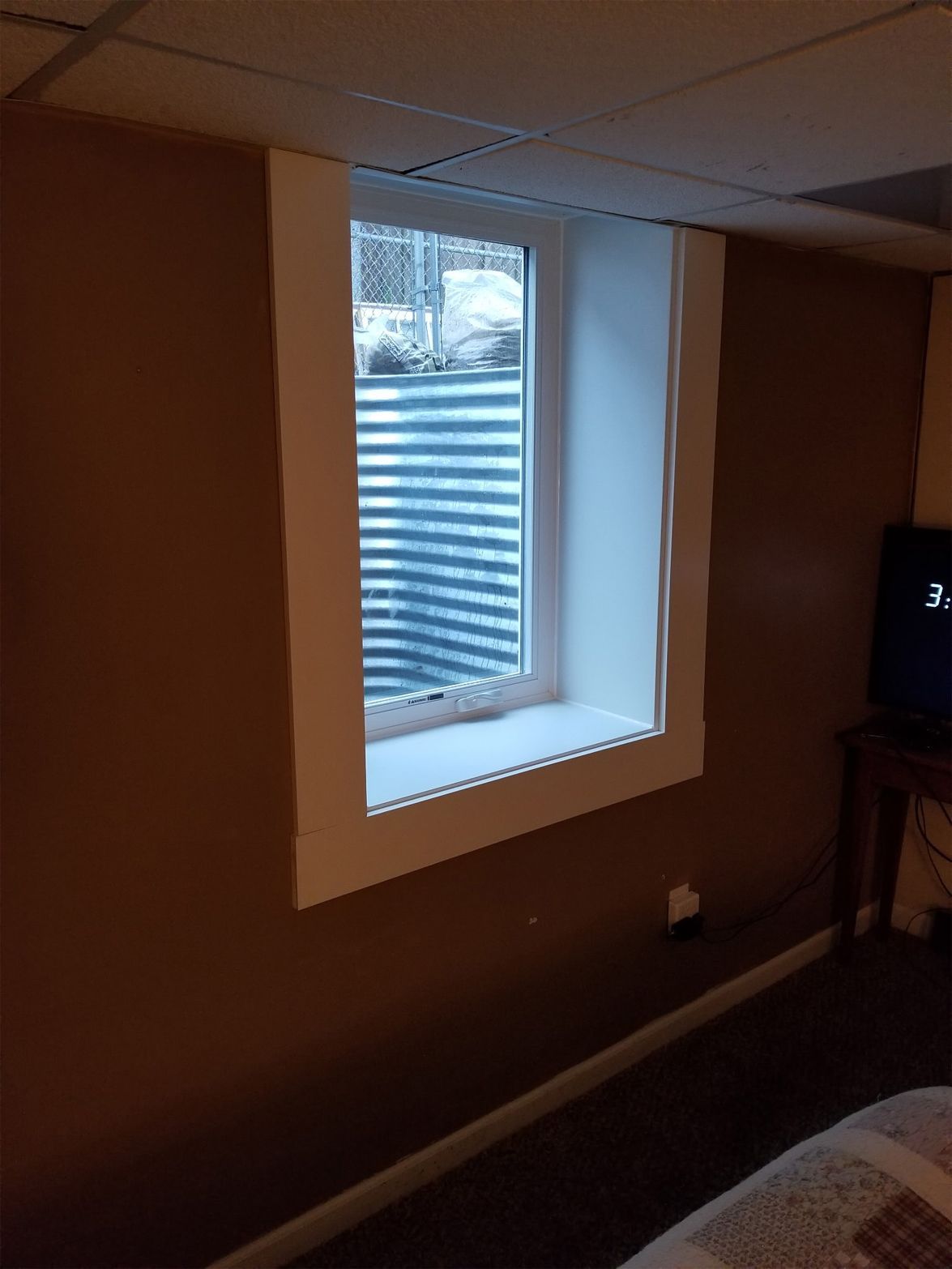 Basement window with white trim, brown walls, and a corrugated metal well.