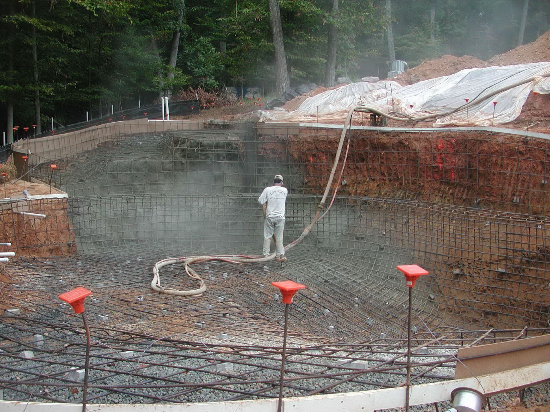 A man is spraying concrete into a pool with a hose.