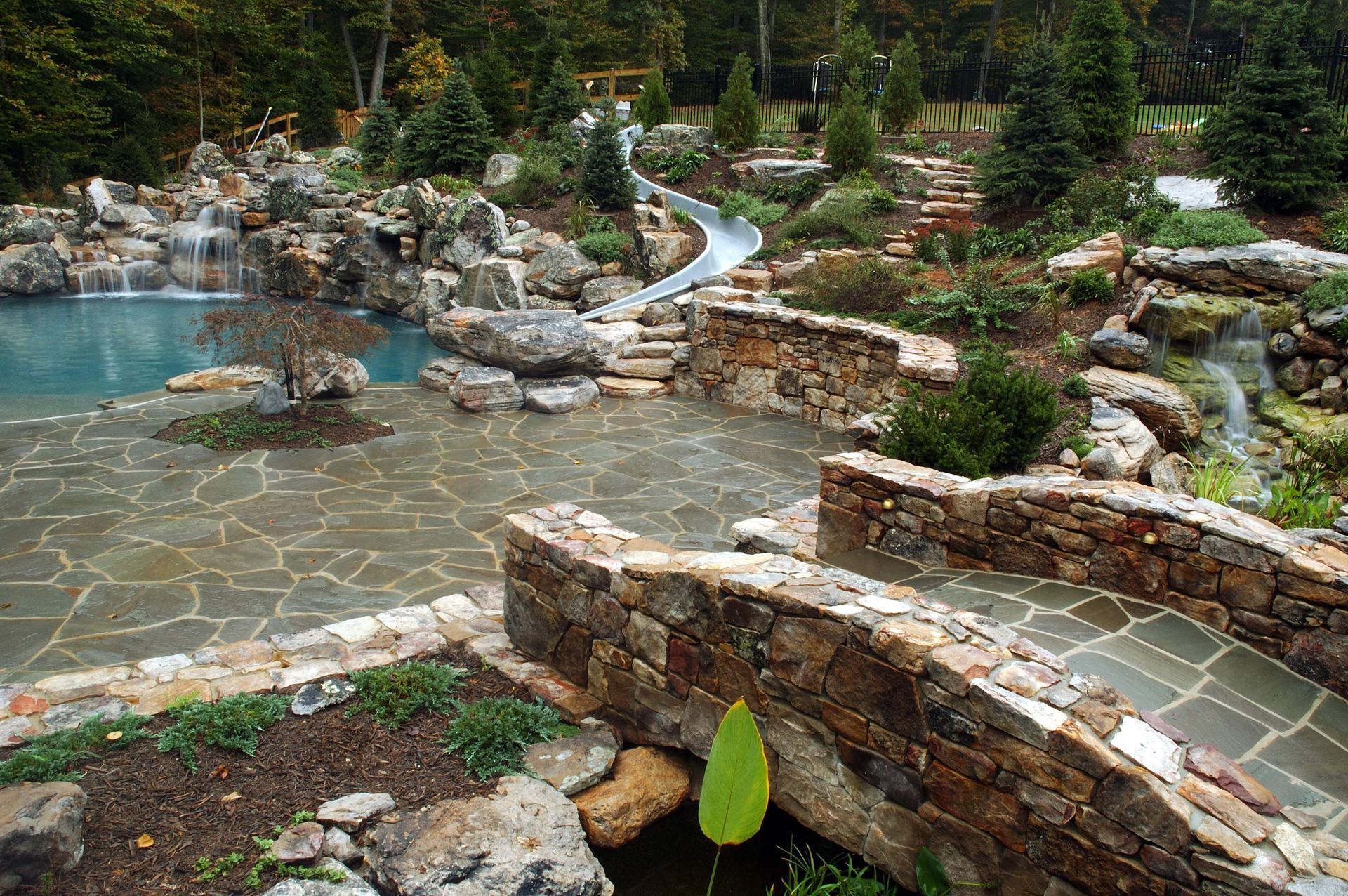 A stone bridge leading to a pool with a water slide in the background
