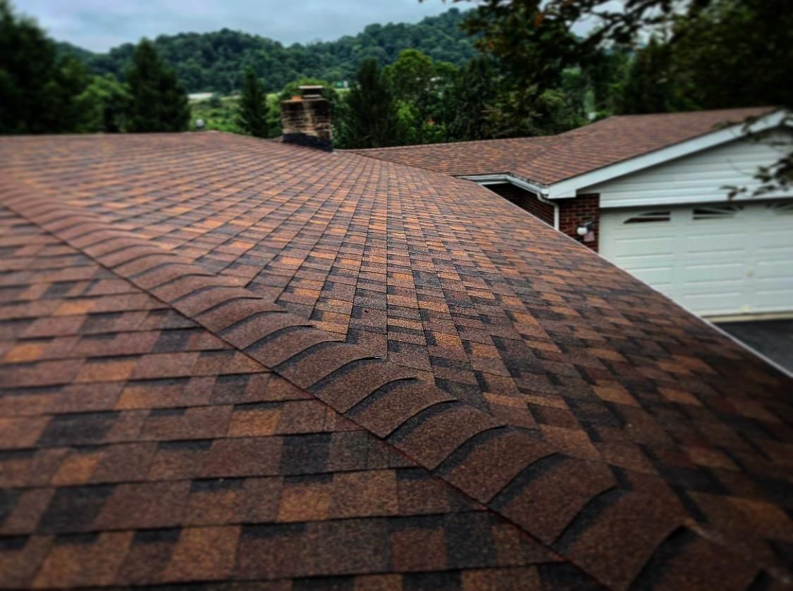 Brown and orange shingle roof with some damage in the center, set against a cloudy sky and trees.