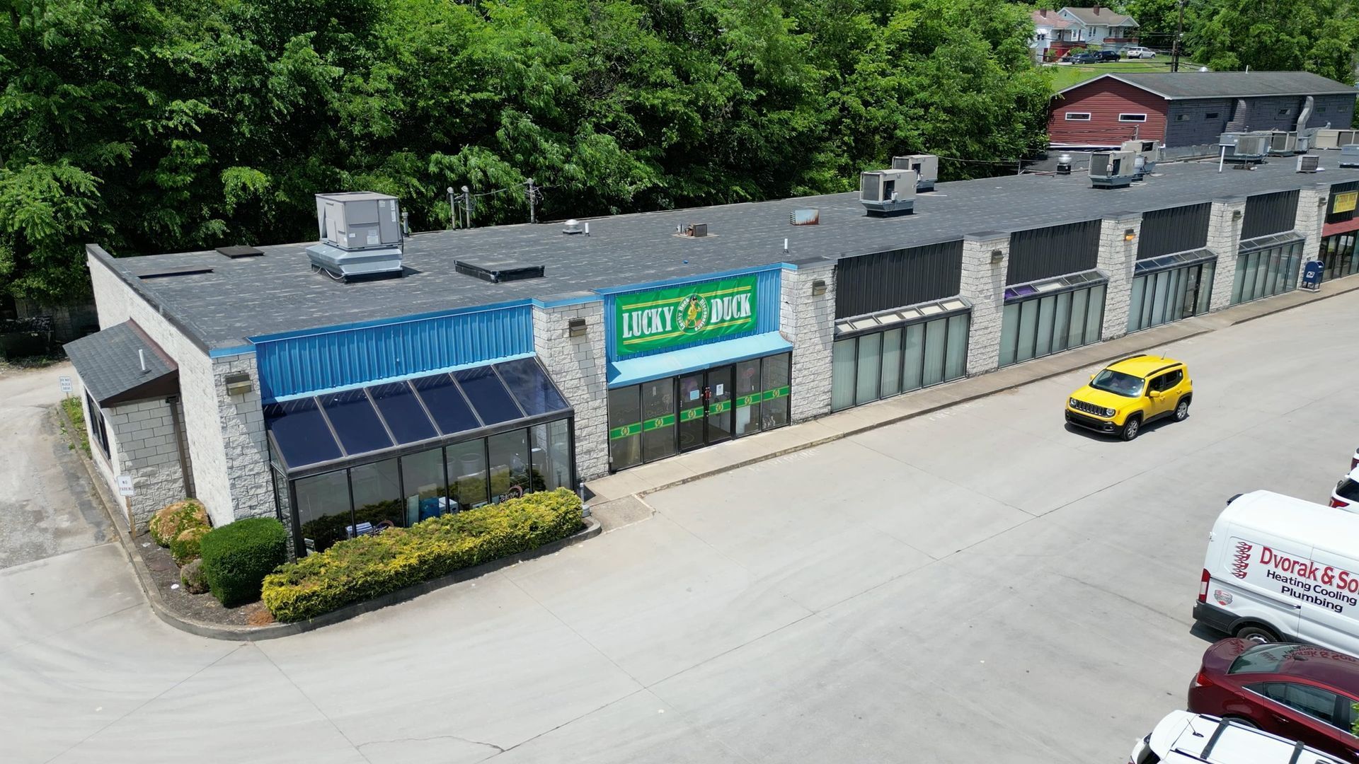 Exterior shot of a long, low strip mall with various storefronts, some painted different colors. A yellow car is parked.