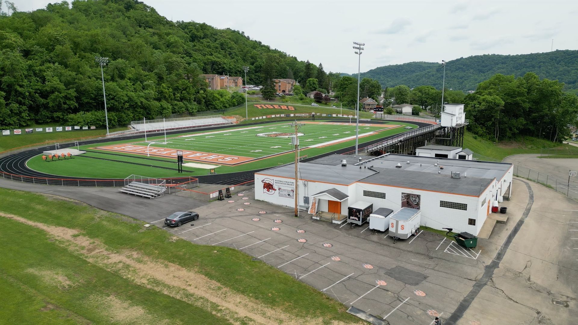 Football field with track, building in foreground, hills in background.