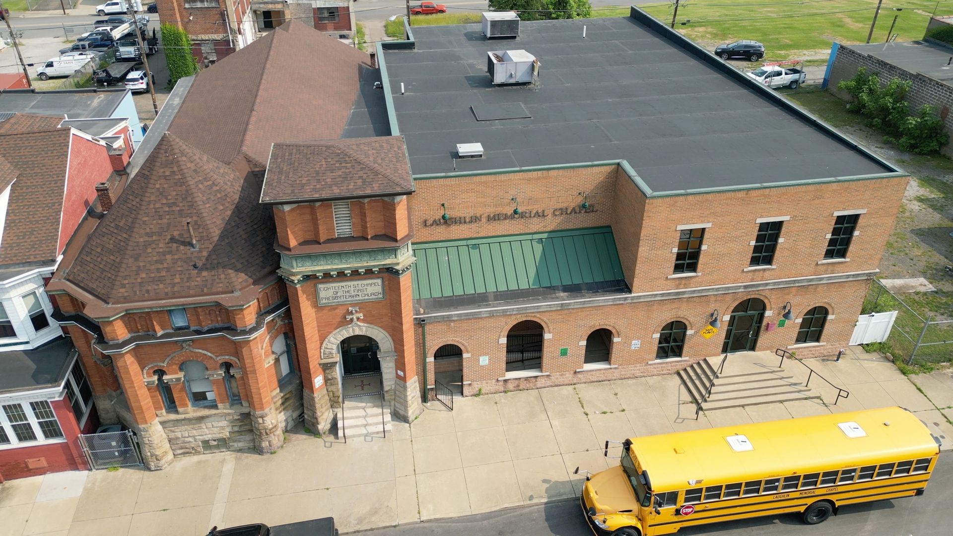 An aerial view of a brick building with a brown roof, next to a school bus.