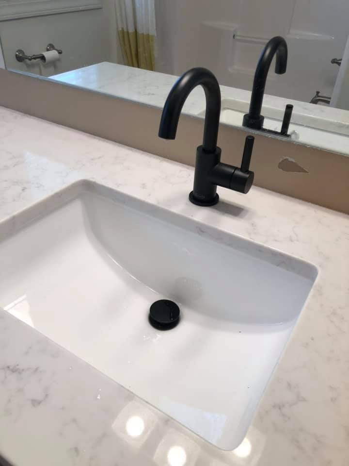 White bathroom sink with black faucet and mirror on a marble countertop