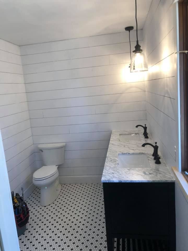 Small white bathroom with toilet, black vanity, marble countertop, wall sconce, and patterned floor tiles.