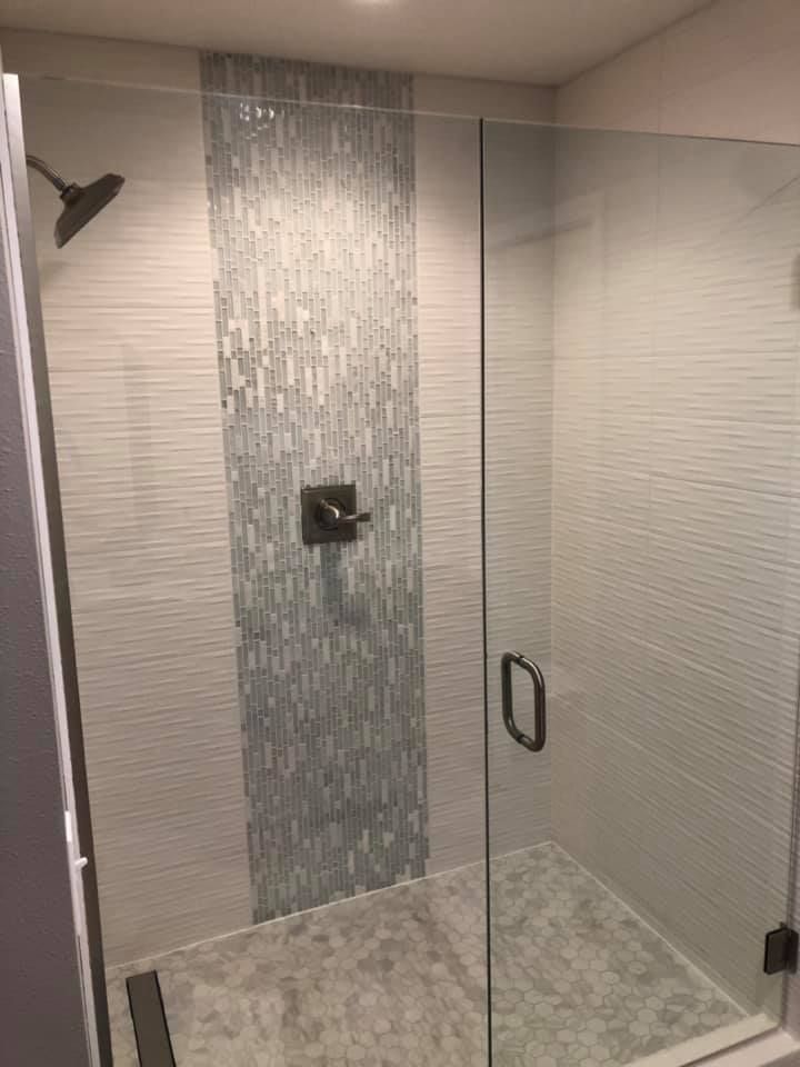 Modern tiled shower with glass door, gray mosaic accent wall, and handheld showerhead