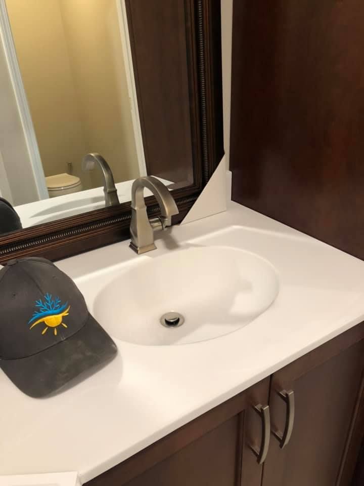 Bathroom sink with chrome faucet, white countertop, mirror, and dark cabinet below.