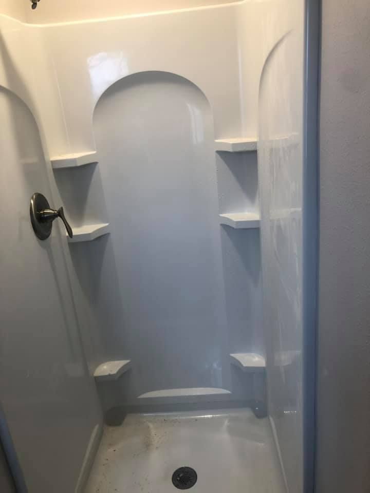 Small white shower stall with built-in shelves, arched alcove, and a round floor drain.