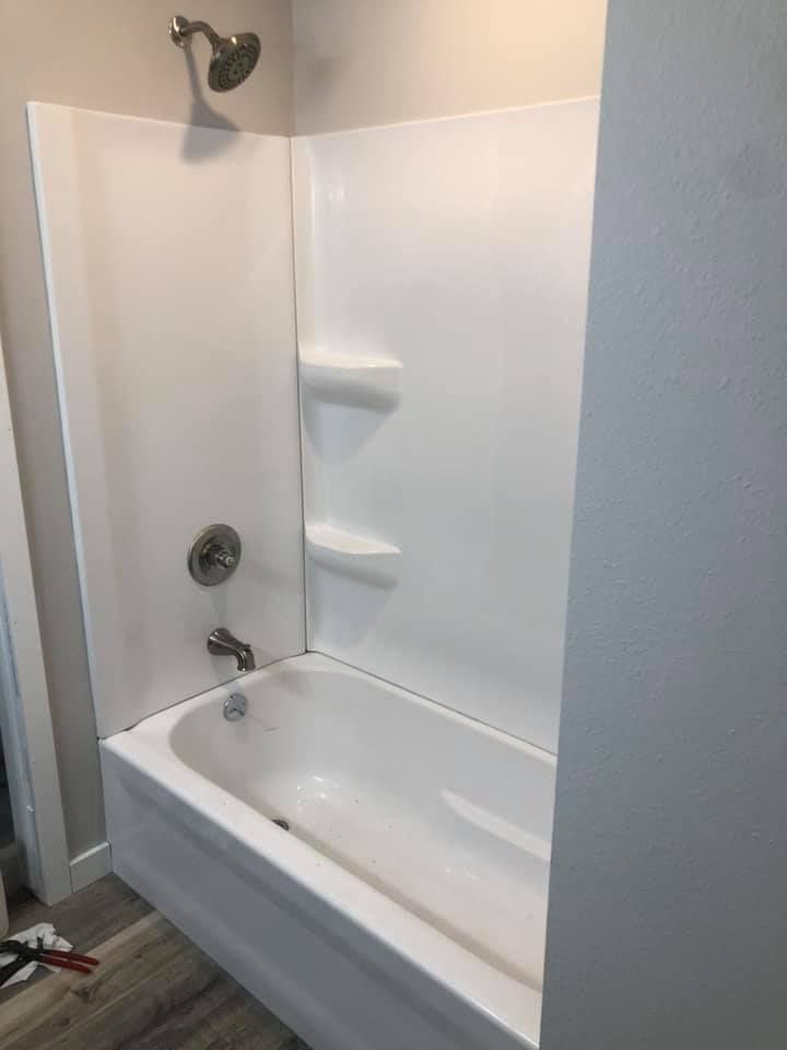 White bathtub and shower with built-in shelves in a bathroom, shown from the corner.