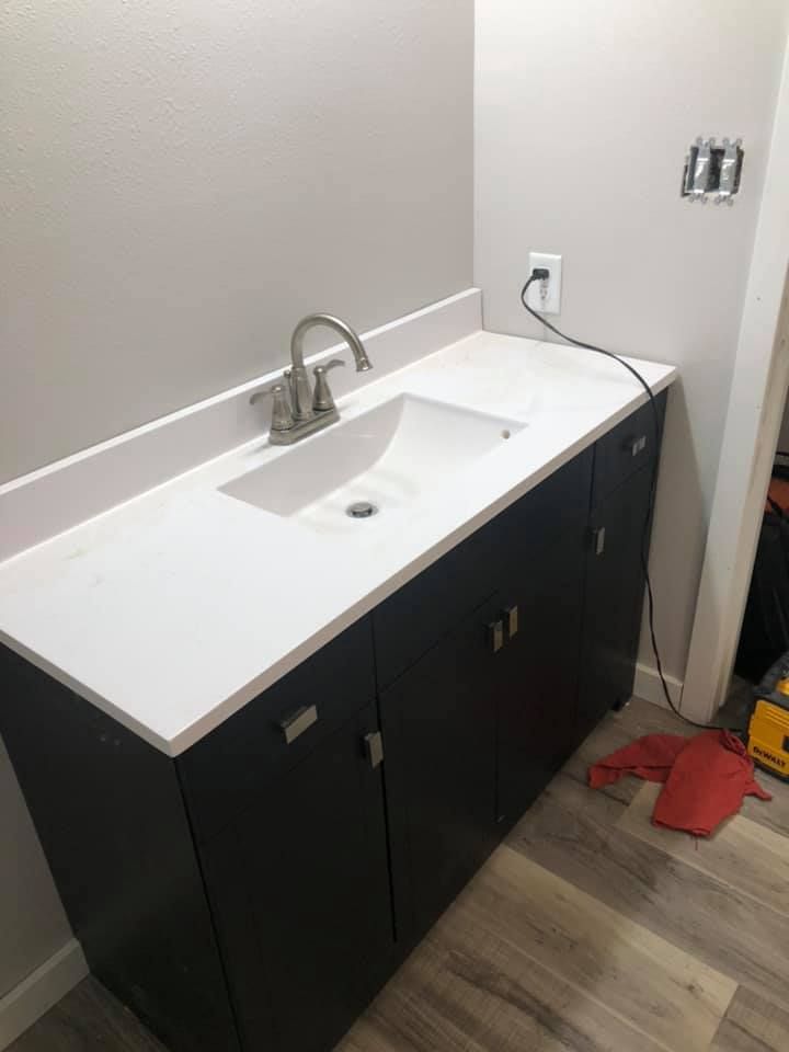 Bathroom vanity with white sink, chrome faucet, and dark cabinets against a light wall.