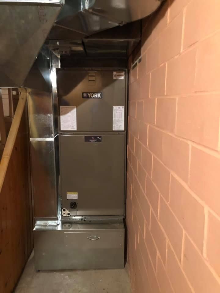 Narrow utility corridor with a large HVAC unit and exposed ductwork beside a brick wall