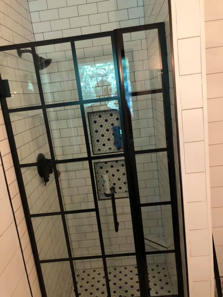 Black-framed glass shower enclosure with white subway tile walls and patterned tile floor.