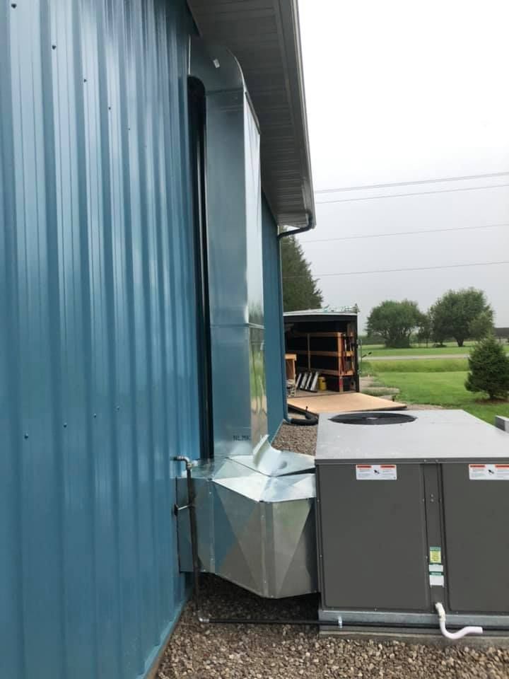 Blue metal building with a silver vent duct beside gray utility boxes in an outdoor industrial yard