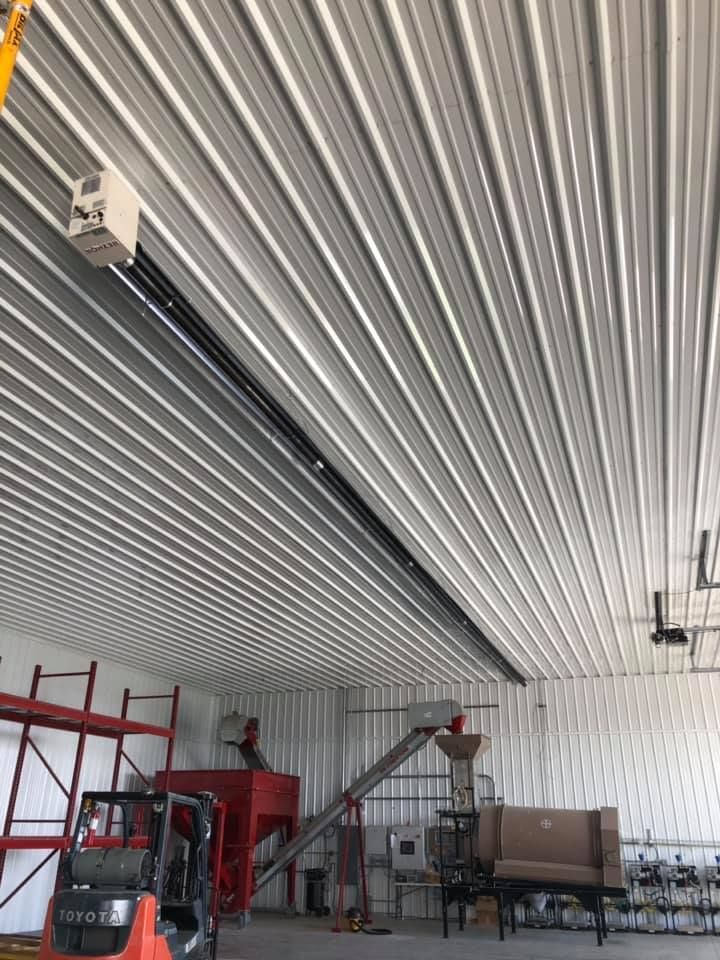Industrial warehouse interior with a striped ceiling, forklift, scaffolding, and equipment on the floor.