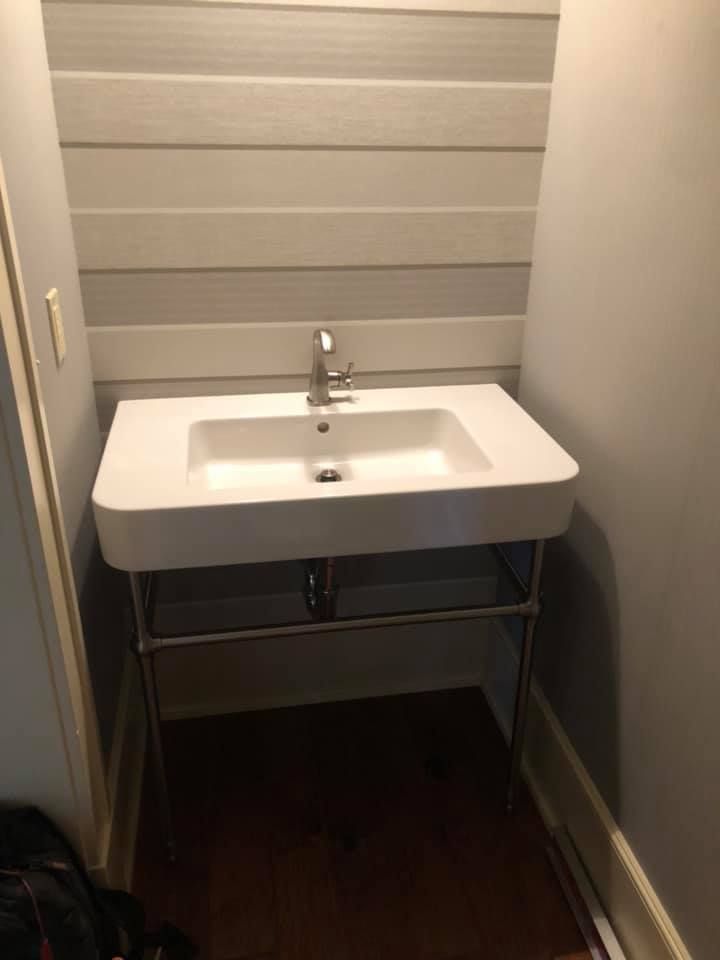Small white bathroom sink with chrome faucet in a narrow alcove, gray walls and dark wood floor.