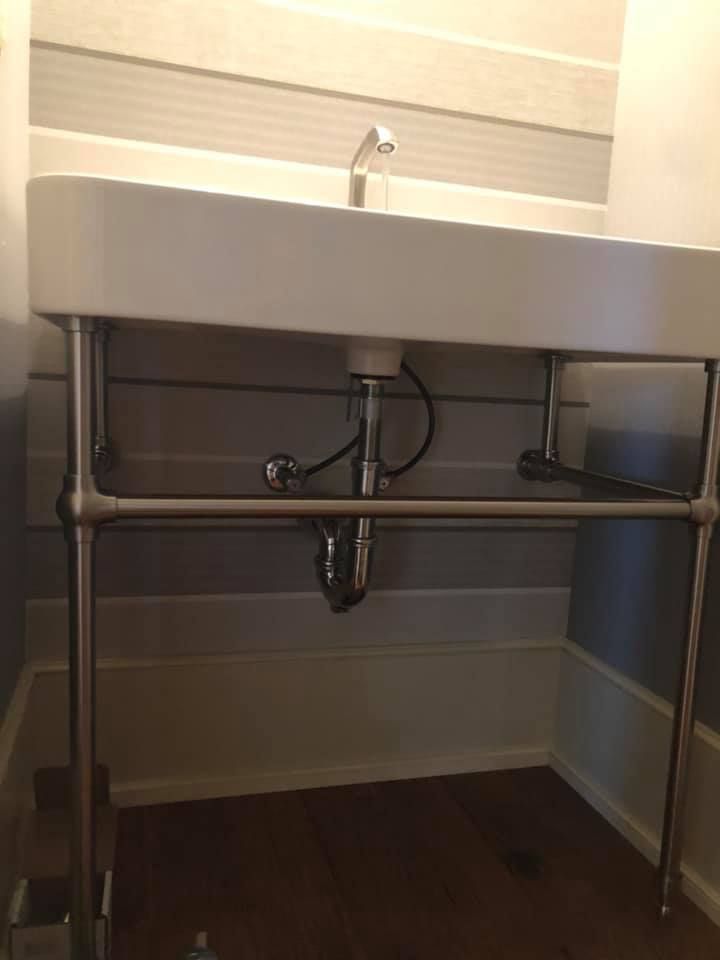 Stainless steel sink and exposed plumbing in a small bathroom or utility room with striped wall tiles.