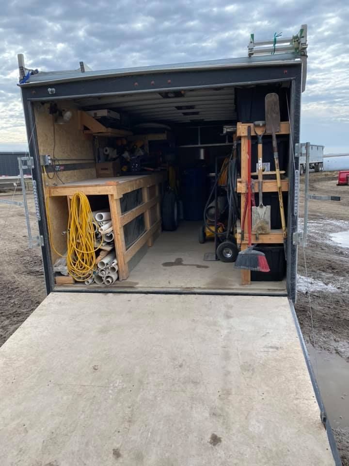 Open trailer with ramp, packed with tools, shelving, and a yellow extension cord inside.