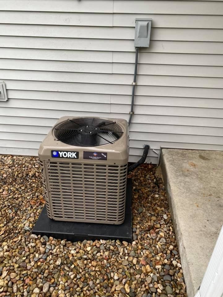Outdoor York air conditioner unit beside a house wall on gravel, with concrete step nearby