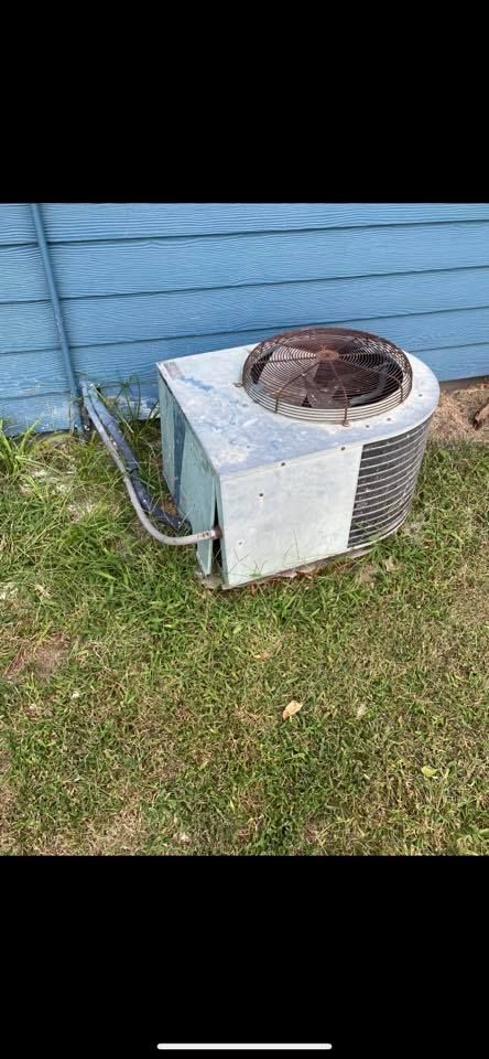 Outdoor air conditioner unit beside a blue house wall on grass, with a rusted top cover