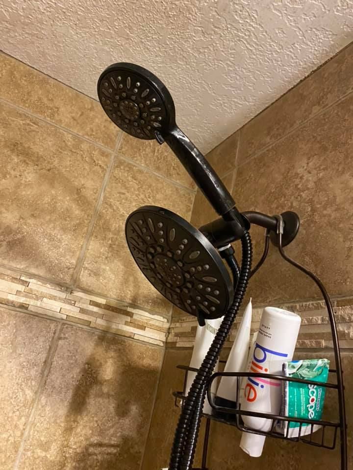 Black showerhead with caddy holding bottles in a beige-tiled shower.