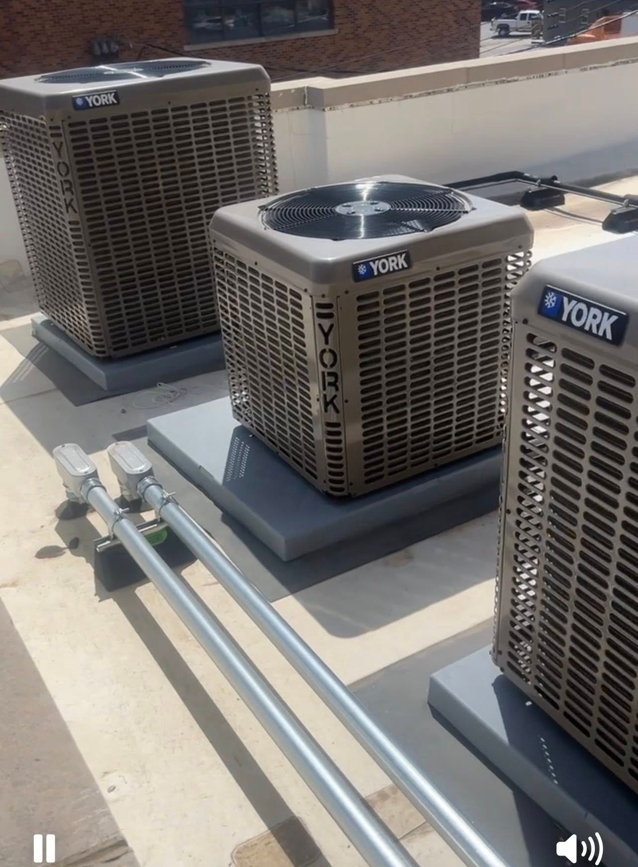 Three rooftop HVAC units with gray metal housings and exposed pipes on a flat roof.
