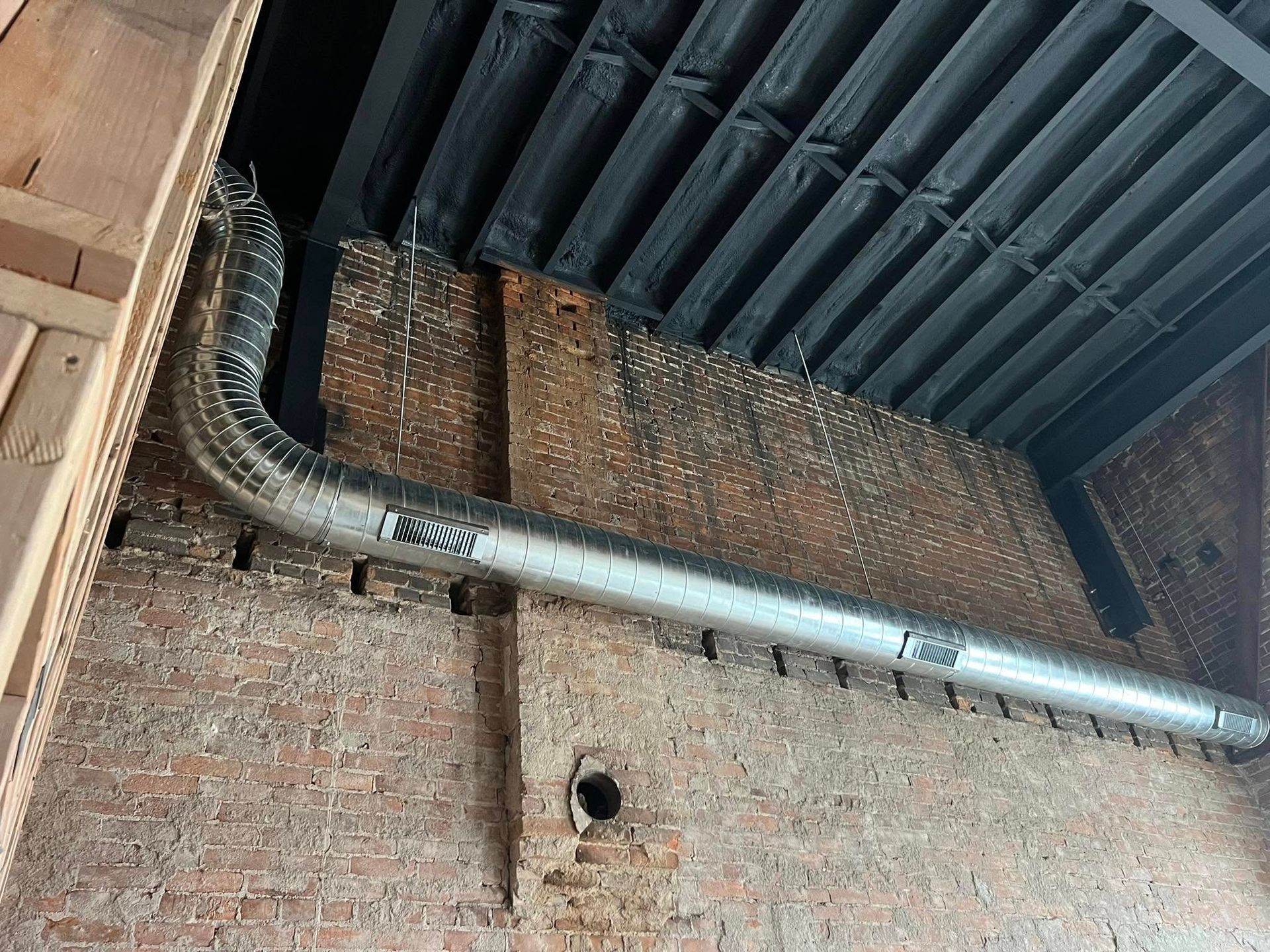 Brick wall with a large silver ventilation duct under a dark corrugated ceiling