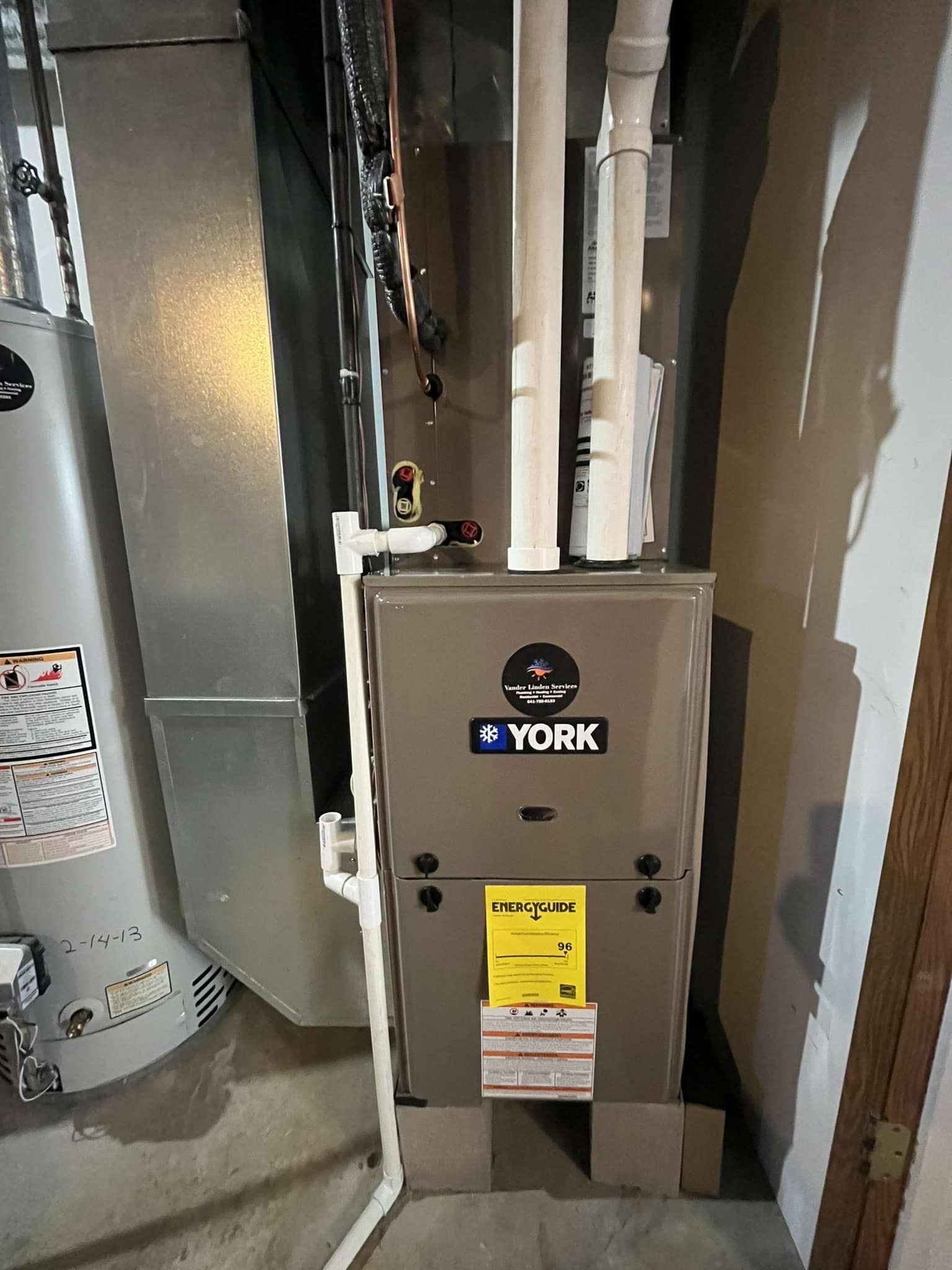 York furnace and nearby water heater in a narrow utility closet with exposed pipes and ducts
