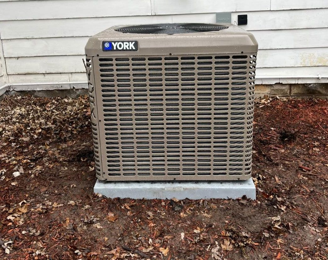 Outdoor York air conditioner unit against a house wall on a bed of mulch and leaves
