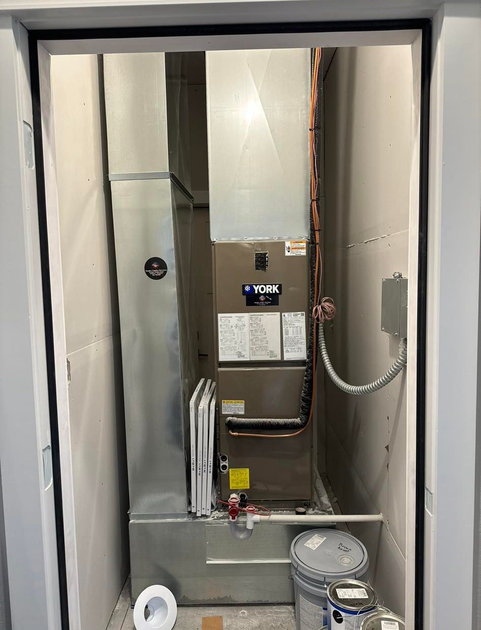 Open HVAC closet with exposed furnace, metal ductwork, and cleaning supplies on the floor