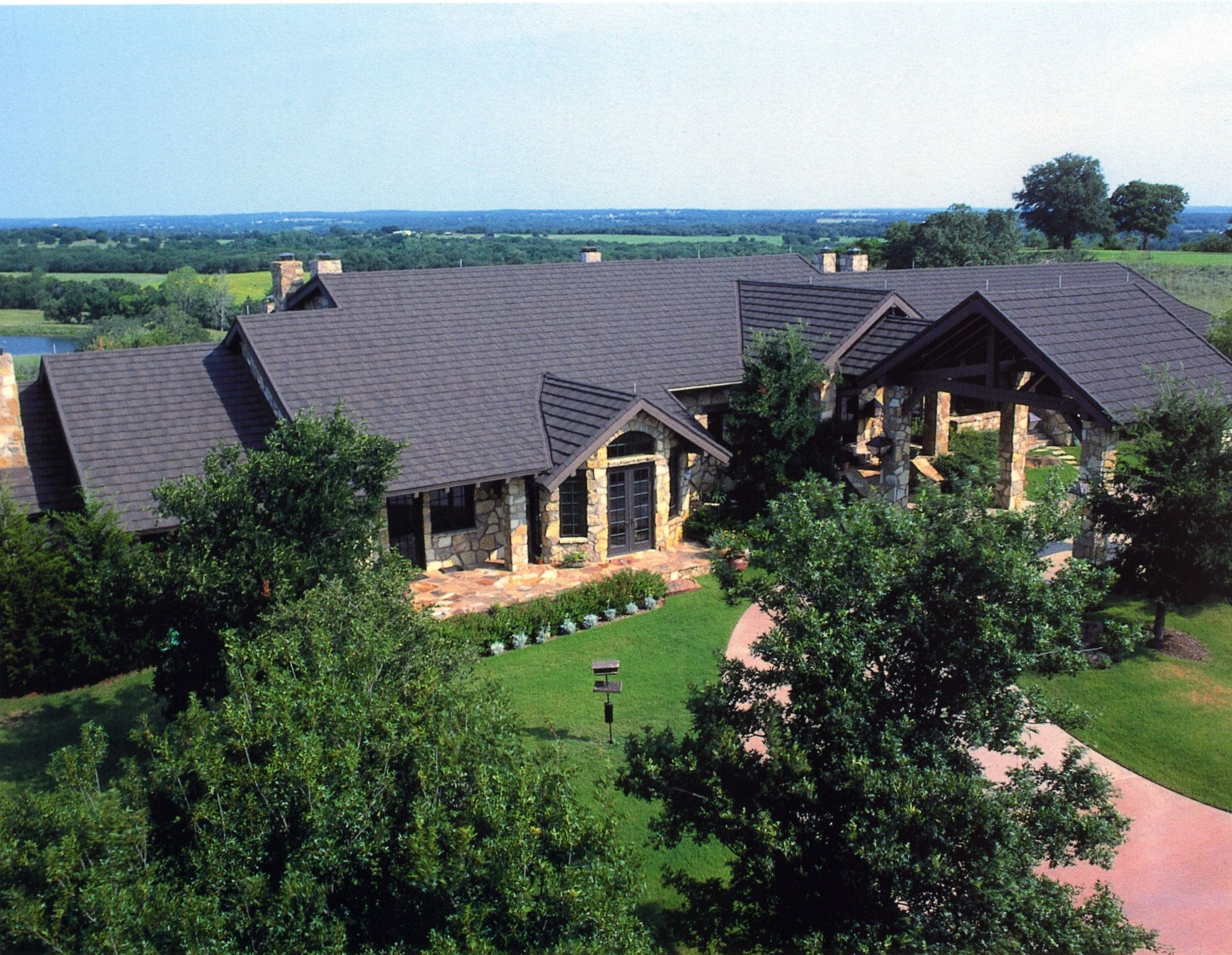 Aerial view of a large lodge with dark roofs, stone walls, and green trees and lawn around it.