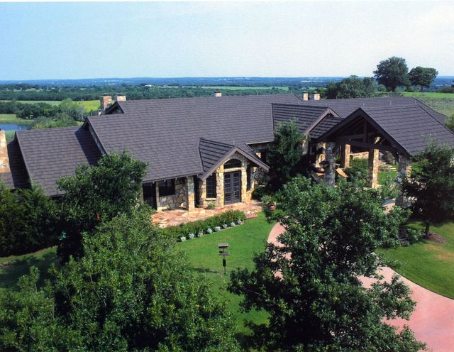 Aerial view of a large building with dark roofs, surrounded by trees and green lawns.