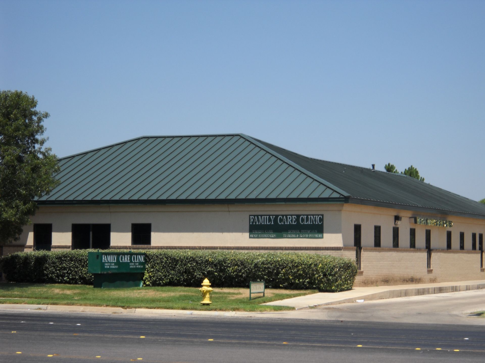 Single-story beige office building with green metal roof and signs along a street.