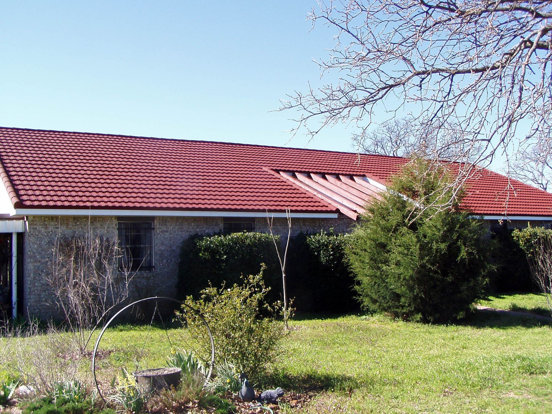 Single-story house with a red roof, green lawn, and trees under a clear blue sky